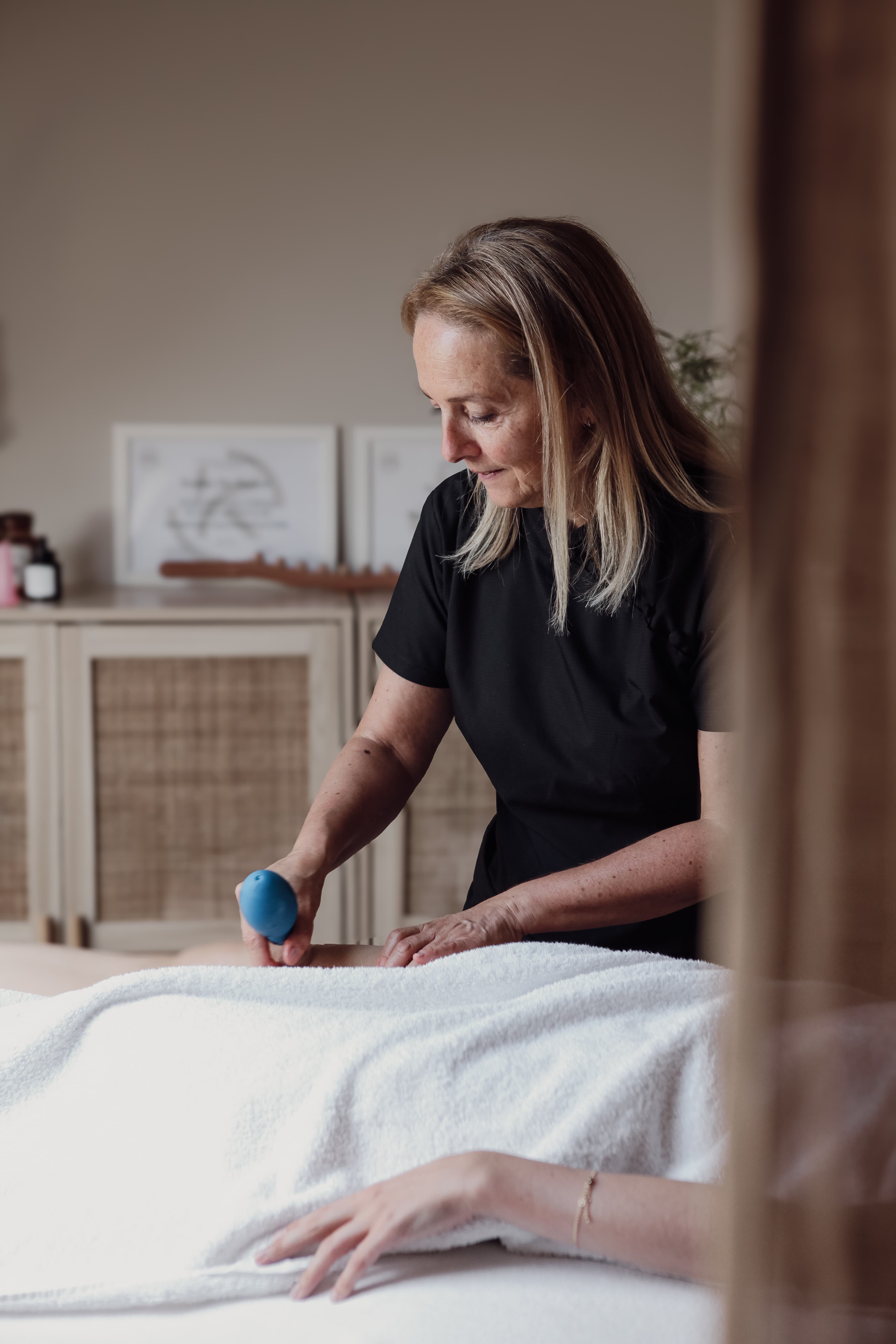 Sophie behandelt een cliënte met een cuppingglas, weids zicht op de praktijkruimte